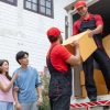 Young couple checks with two movers unloading boxes and furniture from a pickup truck