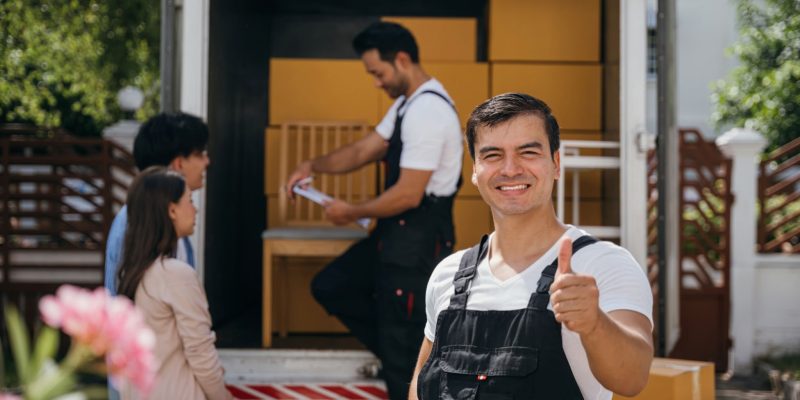 In a portrait a joyful mover unloads boxes from a truck into a new home. These movers display teamwork ensuring efficient relocation and spreading happiness. Moving day concept