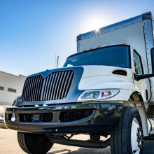 Middle duty Industrial standard white day cab rig semi truck with box trailer for local deliveries and small business needs standing on the wide warehouse parking lot with another trucks